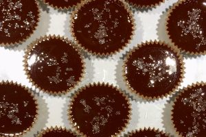 Chocolate Peanut Butter Cups topped with salt lined up on a glass pan