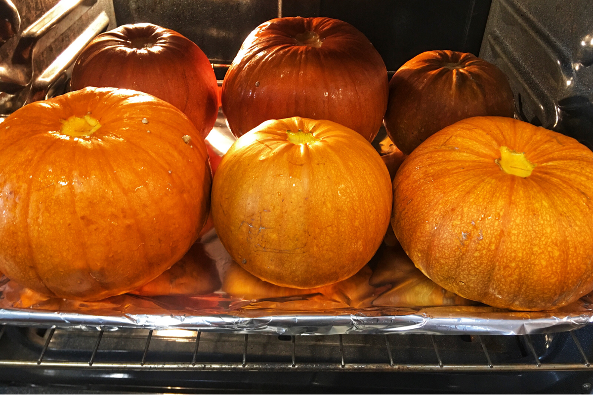 6 pumpkins baking in the oven on a cookie sheet