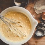 Pancake batter in a white bowl with measuring spoons
