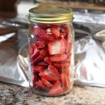 Sliced freeze dried strawberries in a glass jar with mylar bags behind it.
